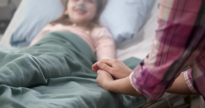 Mother holding child's hand lying in bed in hospital to give encouragement.