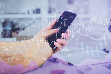 Double exposure of man's hands holding and using a digital device and forex graph drawing. Financial market concept.