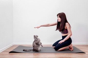 Young Woman Practicing Yoga At Home and Play with Cat on a Mat