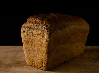Loaf of black rye bread, in the shape of a brick on a wooden board on a black background