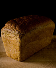 Loaf of black rye bread, in the shape of a brick on a wooden board on a black background
