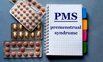 PMS - word in a notebook. Nearby are pills on a gray background