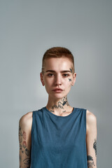 Portrait of tattooed young caucasian woman with short hair and piercing looking at camera while...