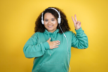 Young african american girl wearing gym clothes and using headphones smiling swearing with hand on...