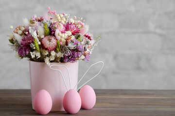 Vase with flowers and Easter eggs, wooden surface, brick wall. Close-up, copy space. The concept of a gentle Easter card