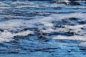 Wavy and foamy water surface; water flowing in the river
