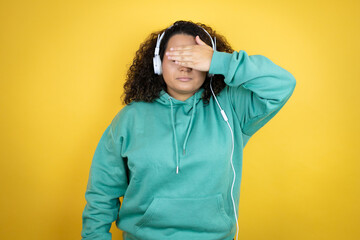 Young african american girl wearing gym clothes and using headphones serious and covering her eyes with her hand