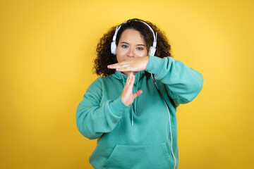Young african american girl wearing gym clothes and using headphones Doing time out gesture with hands, frustrated and serious face