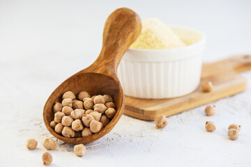Dry chickpeas in a wooden spoon with chickpea flour on a light background.