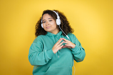 Young african american girl wearing gym clothes and using headphones with Hands together and fingers crossed smiling relaxed and cheerful. Success and optimistic