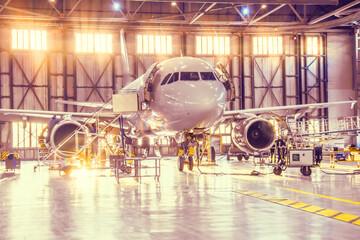 Repair and maintenance of a passenger airliner in an aviation technical hangar, bright light outside the gates.