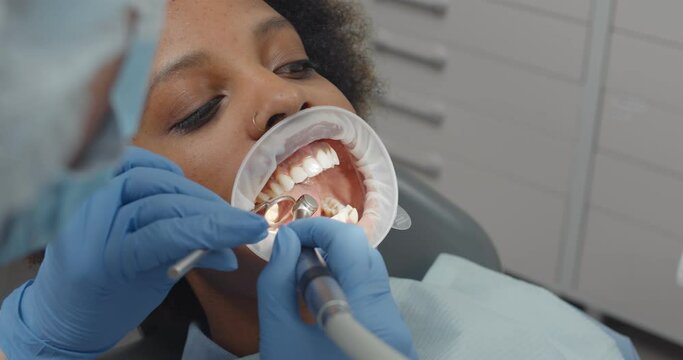 African woman patient with retractor in open mouth checked by dentist