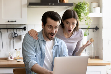 Shocked millennial Caucasian couple look at laptop screen stunned by unexpected news online. Amazed young man and woman spouses surprised by unbelievable good sale deal or discount offer on computer.