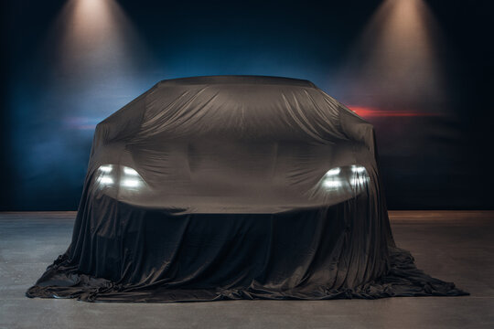 Presentation of the car. Car under the tissue at the autoshow. Brand new car waiting after show and presentation, covered by cloth 