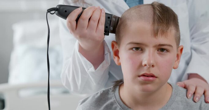 Doctor with hair clipper shaving teen boy preparing for chemotherapy