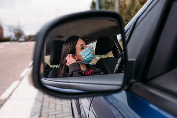 Close up of a young woman is putting a mask on her face sitting in her car