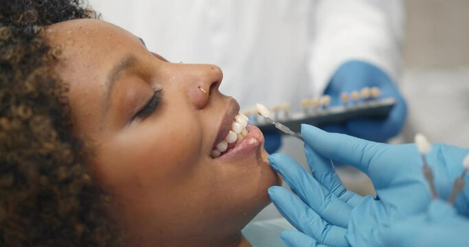 Professional dentist picking perfect shade of white veneers for female patient