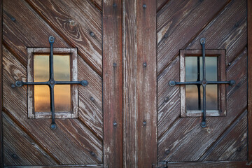 Two small windows at old wooden doors with sunset reflection