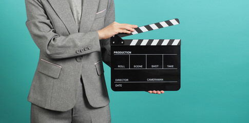 Woman hands holding black Clapperboard or film slate and wear grey suit. it use in videography ,movies and cinema industry on green or Tiffany Blue background.Clapper board for director.