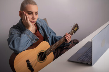 Young woman is learning to play the guitar online. Remote music lessons on a laptop
