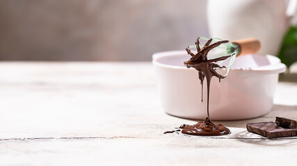 Dark melted chocolate on a whisk in a white bowl on a light background. Handmade chocolate making,...