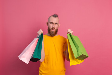 Happy bearded positive man casual look with colorful shopping bags studio pink background