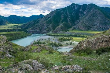 The wide valley of the Katun River. The valley is surrounded by mountains, and in the floodplain of the river there are emerald meadows. There are beautiful islands in the riverbed.
