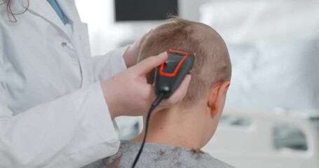 Back view of kid sitting in hospital ward and having hair cut preparing for brain surgery