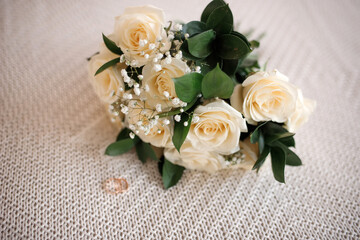 Wedding rings near a wedding bouquet of red and white roses.