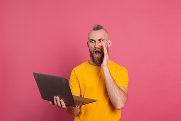 Bearded man with laptop isolated shock emotions screaming on pink background