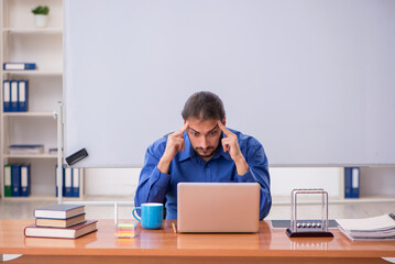 Young male teacher physicist sitting in the classroom