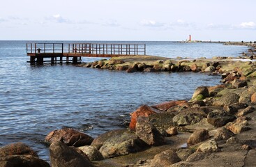 Rocky coast at promenade and pier in Mangalsala ending with red lighthouse, located at Riga sea...