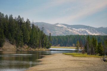 A lake running through Yellowstone National Park with pine trees and mountains.