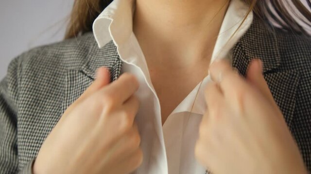 The girl adjusts her jacket and collar. White shirt, gray pajama top. Close-up. Getting ready, getting dressed for work. Look good. Smooth it out.
