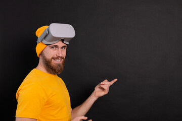 Cheerful handsome positive man  in vr glasses point to left  with hands studio black background