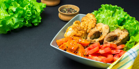 Baked fish with vegetables on a dark background. Copy space. Side view.