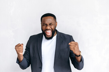 Emotional excited African American male entrepreneur, freelancer or student in stylish suit,...