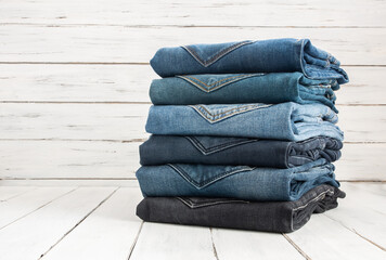 Stack of various denim jeans, trousers on stone wooden rustic background, fashion design 
