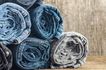 Stack of various denim jeans, trousers on stone wooden rustic background, fashion design 