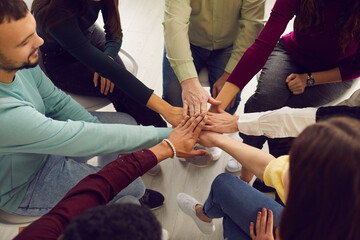 From above view of diverse senior and young people sitting in circle and putting hands together in community meeting or group therapy session. Concept of support, unity, success, help and trust