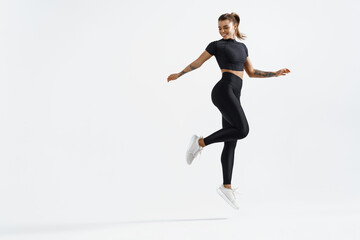 Fit and healthy sports woman runner jumping and looking behind. Female athlete in workout clothing doing exercises on white background, staring at empty space