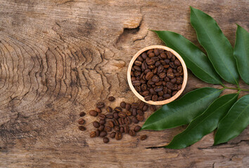 Top view of Coffee beans in the wooden bowl and the leaves of the coffee plant are placed on the wooden table. 