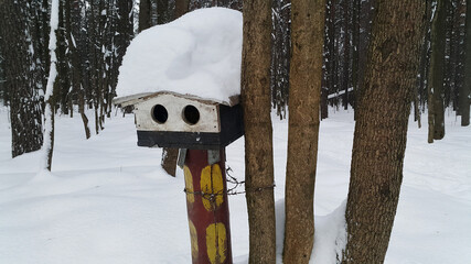 Snow-covered bird feeder with two holes. There is no bird near wooden bird feeder. Winter in Timiriazevsky city park in Moscow, Russia.
