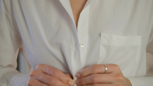 A young woman puts on a shirt, fastens a button close-up. White shirt. Businessman. Getting ready, getting dressed for work. Business style. Classic clothing.