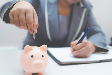 business woman putting coin in to piggy bank with calculate and note on paper account for...