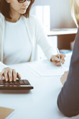 Accountant checking financial statement or counting by calculator income for tax form, hands close-up. Business woman sitting and working with colleague at the desk in office. Audit concept