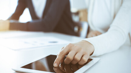 Businesswoman pointing at tablet computer screen while giving presentation to her female colleague. Group of business people working at the desk in office. Teamwork concept