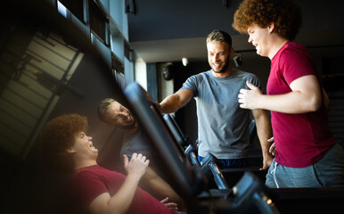 Fat young men with trainer exercising at fitness gym.
