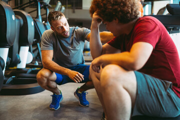 Overweight young man exercising gym with personal trainer
