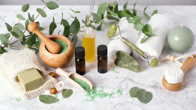 Woman hand pouring skin care oil or serum drops with pipette dropper. Spa, wellness and beauty products: gua sha, face roller. Natural aromatherapy with eucalyptus essential oils and bath salts